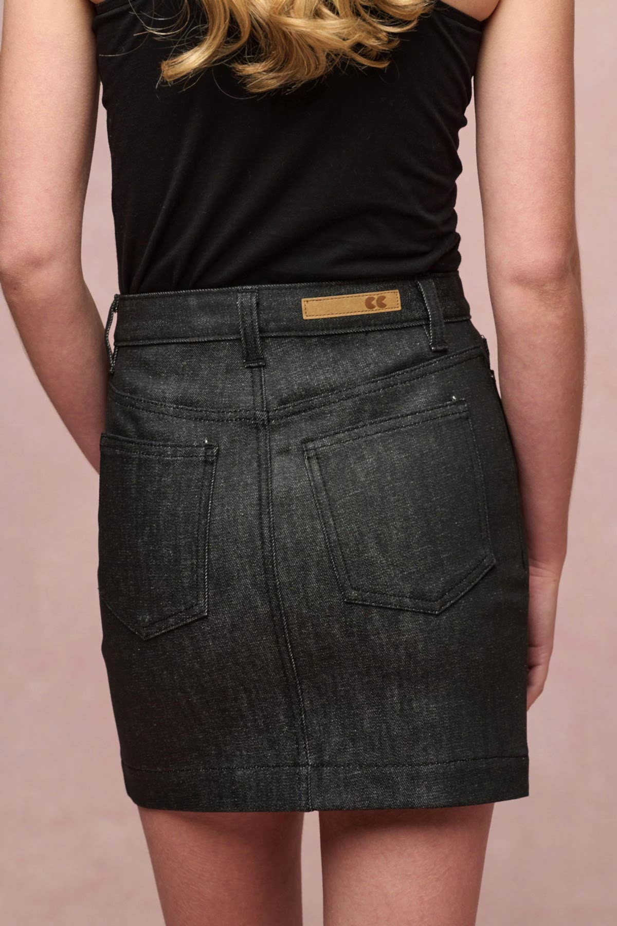 Image showing a close up of the back of Charlie denim mini skirt in black. Two back pockets, belt loops and CC logo jean patch on the waistband