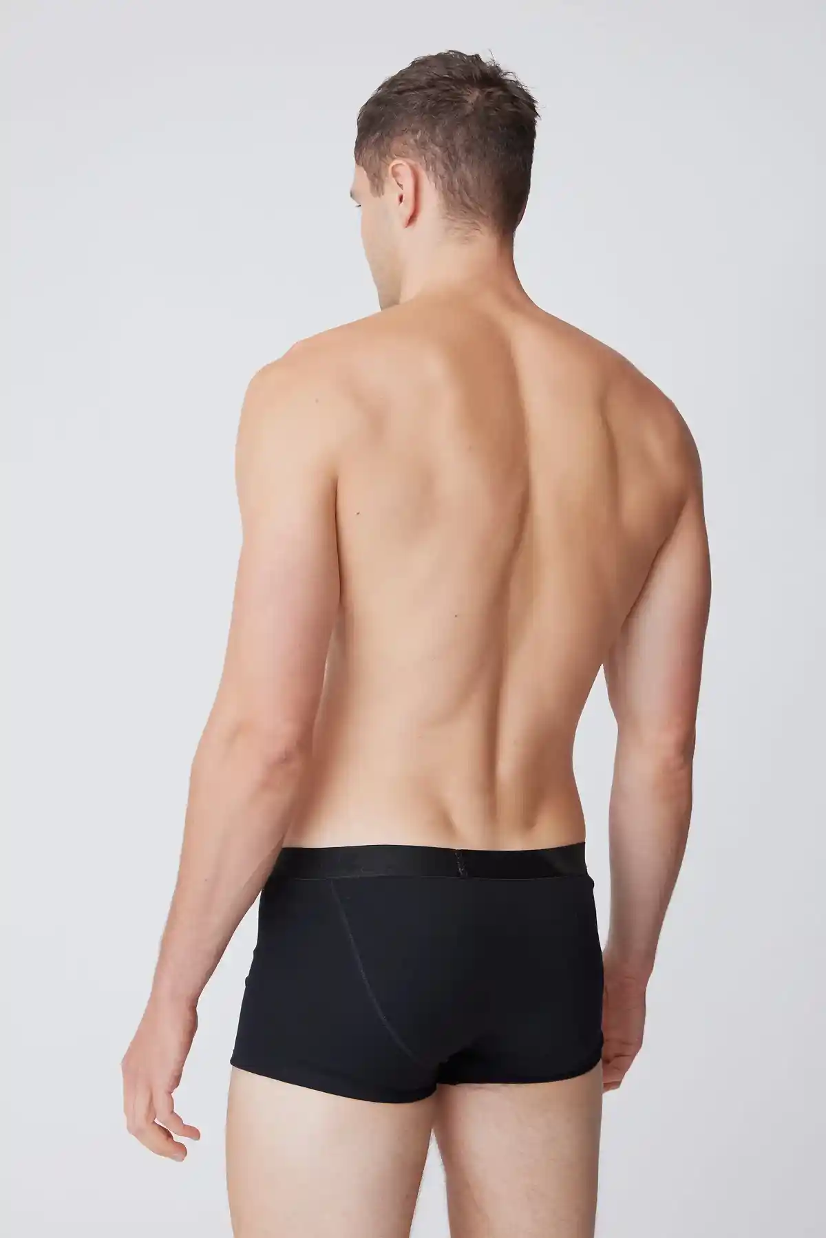 White male facing away wearing black trunks 