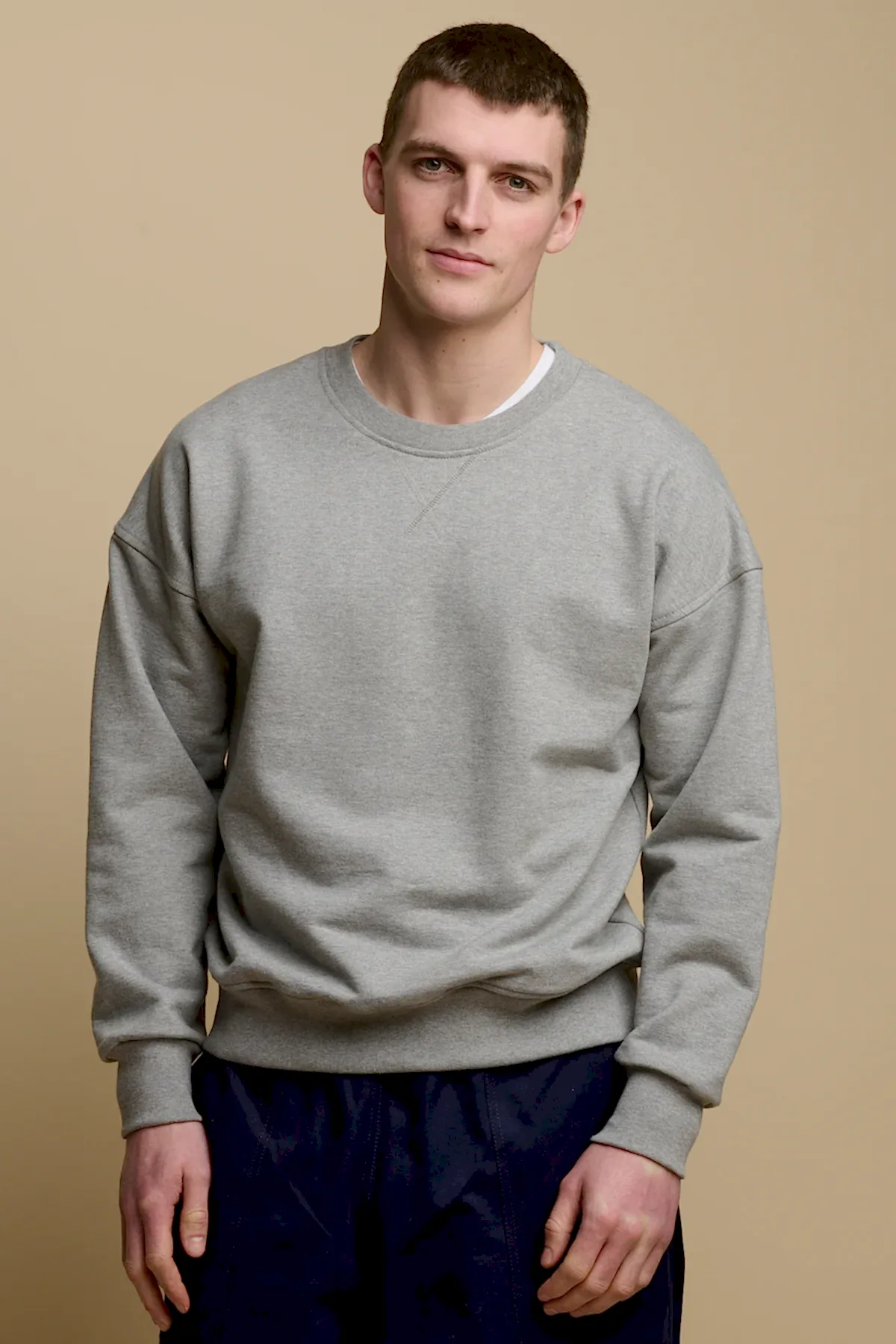 Thigh up front of brunet male wearing men's heritage drop shoulder sweatshirt in grey, worn over crew neck white t shirt paired with cameraman pants in navy